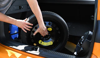 Person lifting a spare wheel out of a car's boot