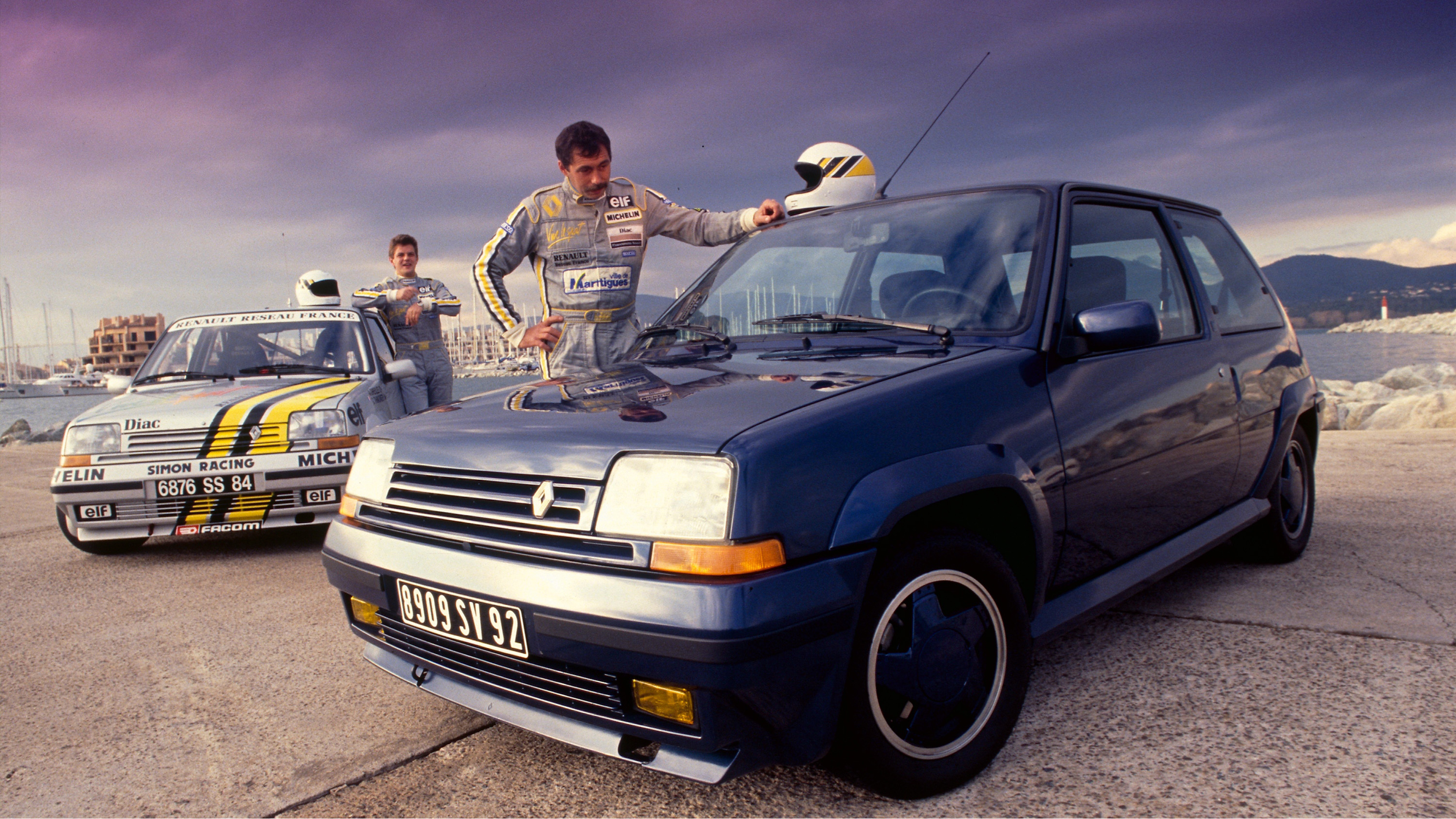 Racing drivers standing next to two Renault 5 GTs