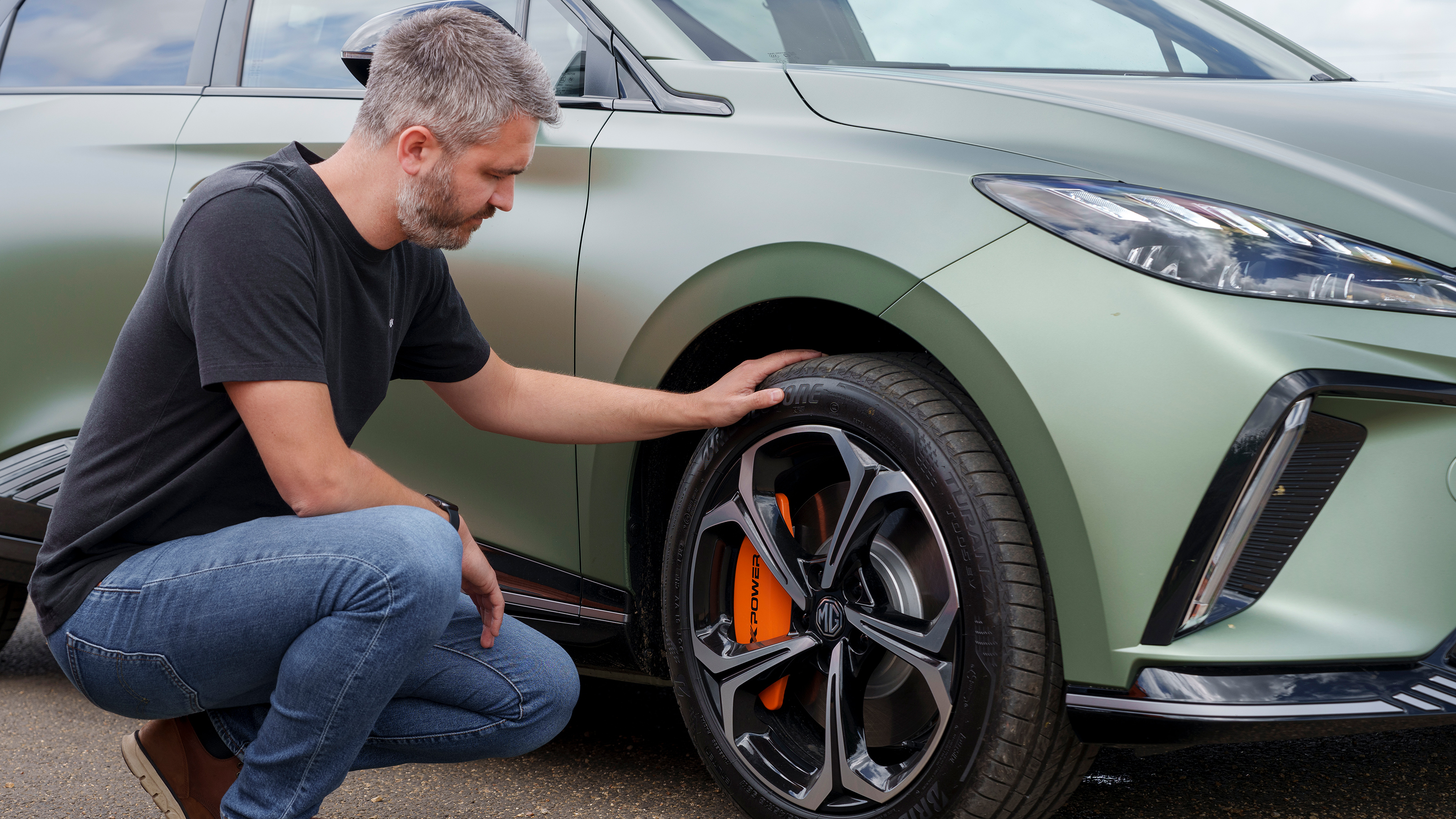 Carbuyer and DrivingElectric editor Richard Ingram inspecting the MG4 XPower's front offside wheel