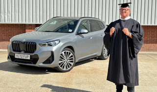 Auto Express special contributor Steve Sutcliffe dressed in a graduation cap and gown, standing next to our long-term BMW X1