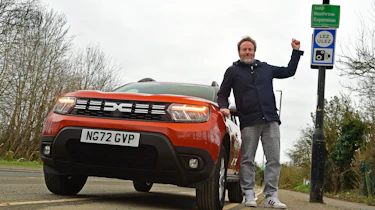 Auto Express web producer Pete Baiden standing next to the Dacia Duster and a ULEZ road sign