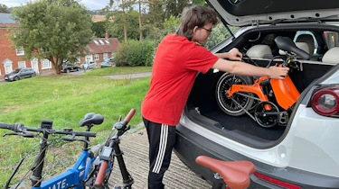 Person loading a folding e-bike into a car boot