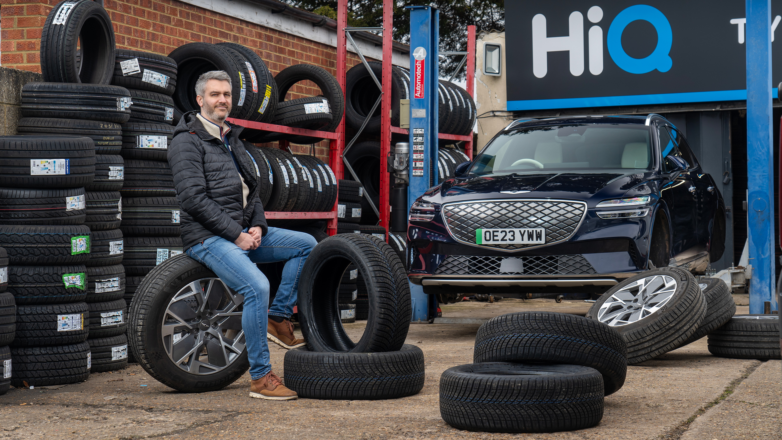 Auto Express deputy editor Richard Ingram sitting in a HiQ tyre changing workshop next to the Genesis Electrified GV70