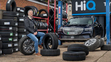 Auto Express deputy editor Richard Ingram sitting in a HiQ tyre changing workshop next to the Genesis Electrified GV70