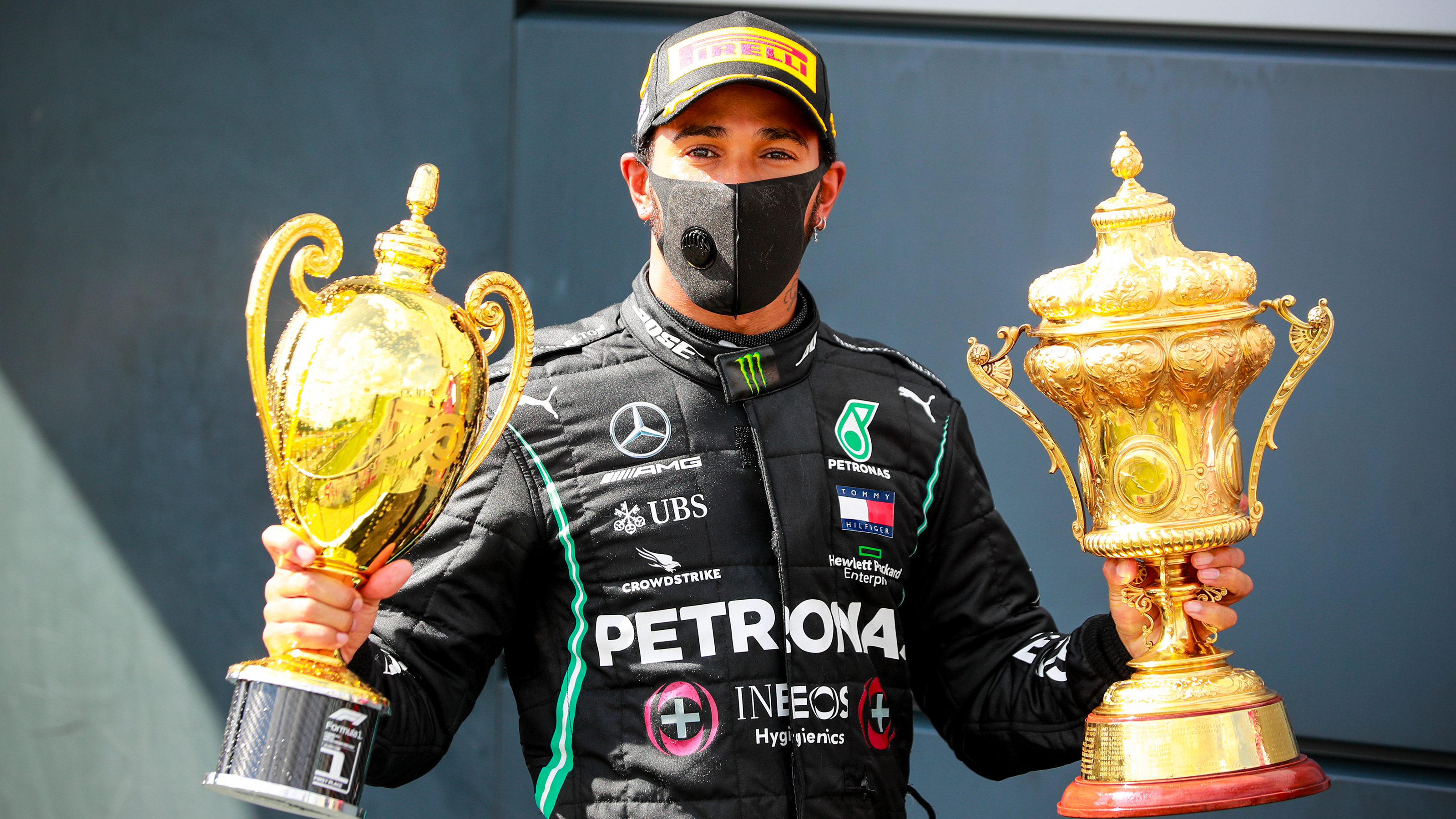 Lewis Hamilton sitting holding two trophies