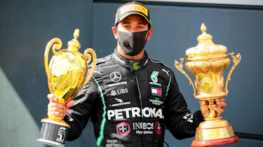 Lewis Hamilton sitting holding two trophies