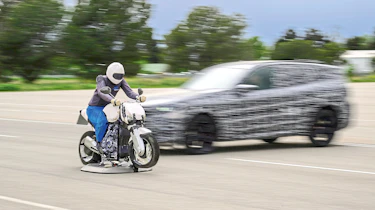 BMW X3 prototype (camouflaged) and dummy test car driving towards a motorcycle crash test dummy