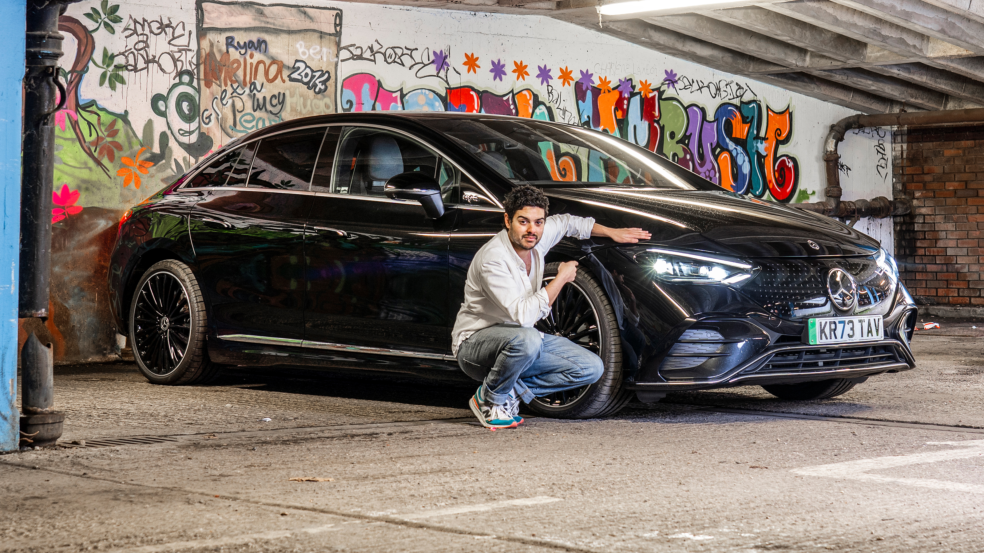 Auto Express senior staff writer Jordan Katsianis crouching next to the Mercedes EQE