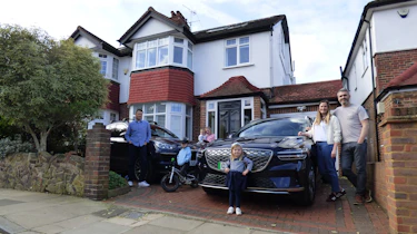 Auto express deputy editor Richard Ingram standing with the Genesis Electrified GV70 and Porsche Cayenne