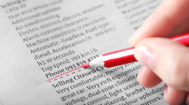 Person underlining a telephone number on a used car adevrt