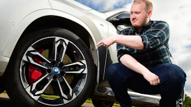 Auto Express news reporter Ellis Hyde leaning pointing at the BMW iX1's wheel