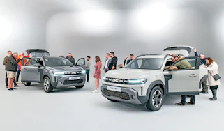 Group of Dacia Duster owners standing in a room with two brand-new Dacia Dusters