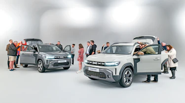 Group of Dacia Duster owners standing in a room with two brand-new Dacia Dusters