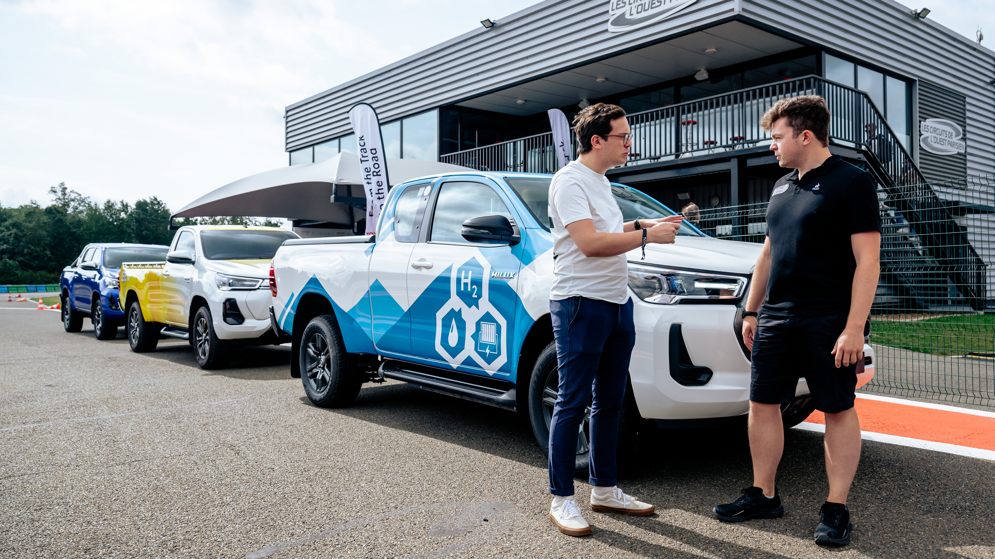 Hydrogen fuel-cell powered Toyota Hilux with Auto Express consumer reporter Tom Jervis talking to a Toyota engineer in front of some pick-up trucks