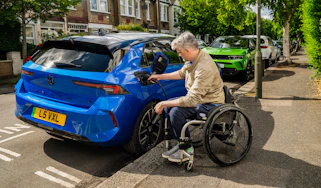 Wheelchair user plugging a charging cable into a Vauxhall Astra Electric