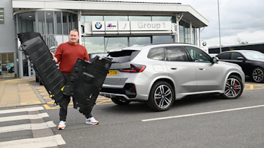 Auto Express news reporter Ellis Hyde holding two BMW iX1 undertrays