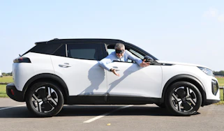Auto Express deputy editor Richard Ingram leaning out of the Peugeot E-2008 while wearing a blindfold