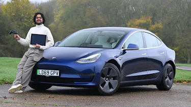 Auto Express senior staff writer Jordan Katsianis holding a laptop and leaning on a Tesla Model 3