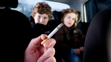 Person smoking in car in front of children