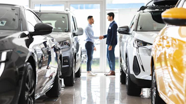 Two people shaking hands in between a collection of cars