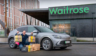 Auto Express chief sub-editor Andy Pringle crouching next to the Genesis GV60 while parked outside a Waitrose store