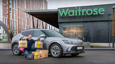 Auto Express chief sub-editor Andy Pringle crouching next to the Genesis GV60 while parked outside a Waitrose store