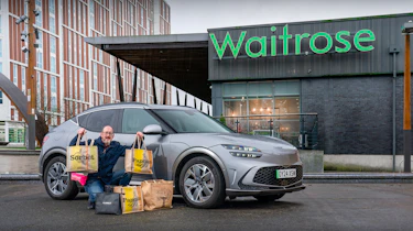 Auto Express chief sub-editor Andy Pringle crouching next to the Genesis GV60 while parked outside a Waitrose store