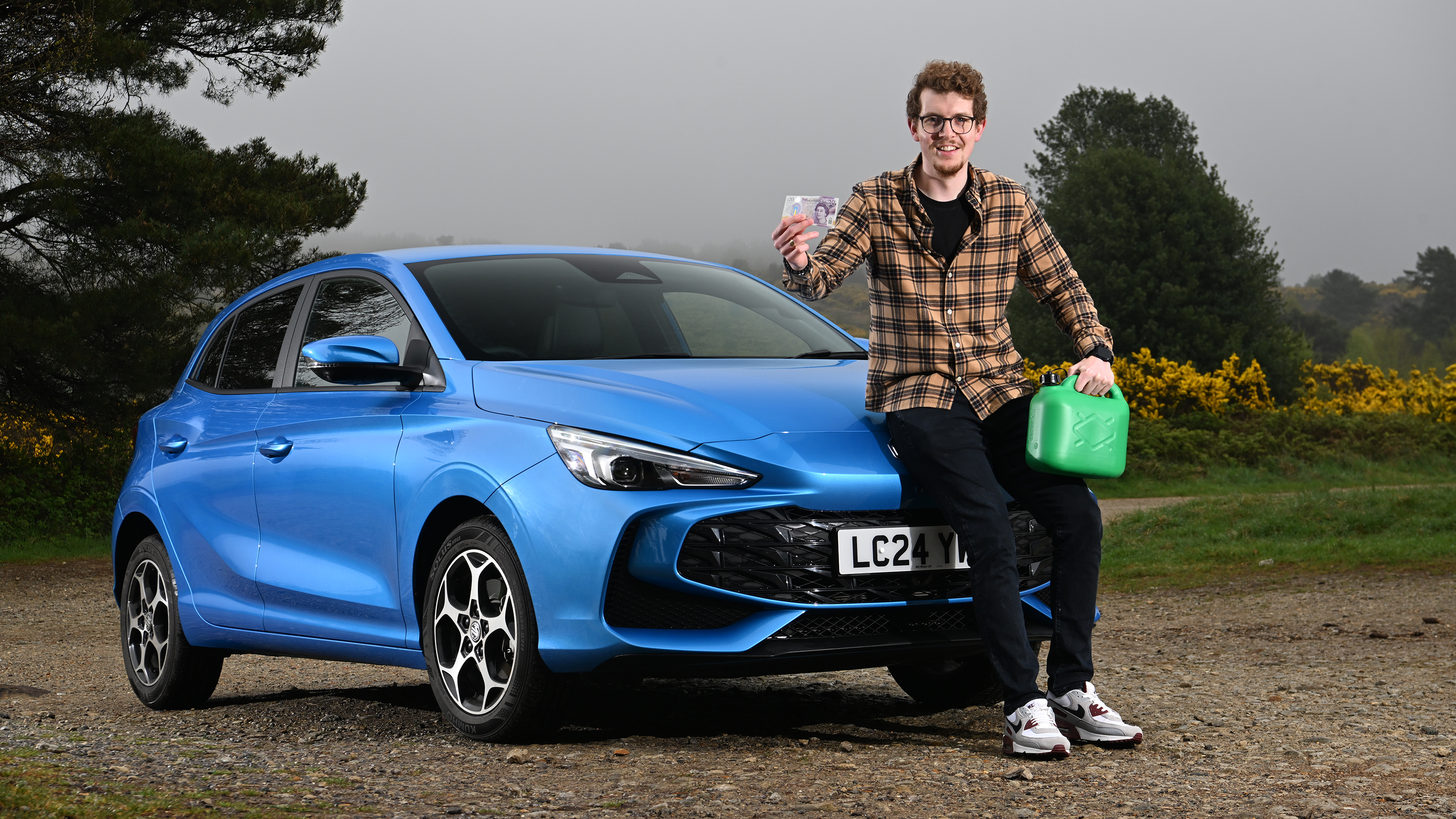 Auto Express content editor Ryan Birch sitting on the MG3's bonnet while holding a pound note and a gerry can