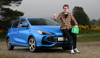 Auto Express content editor Ryan Birch sitting on the MG3's bonnet while holding a pound note and a gerry can