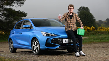 Auto Express content editor Ryan Birch sitting on the MG3's bonnet while holding a pound note and a gerry can