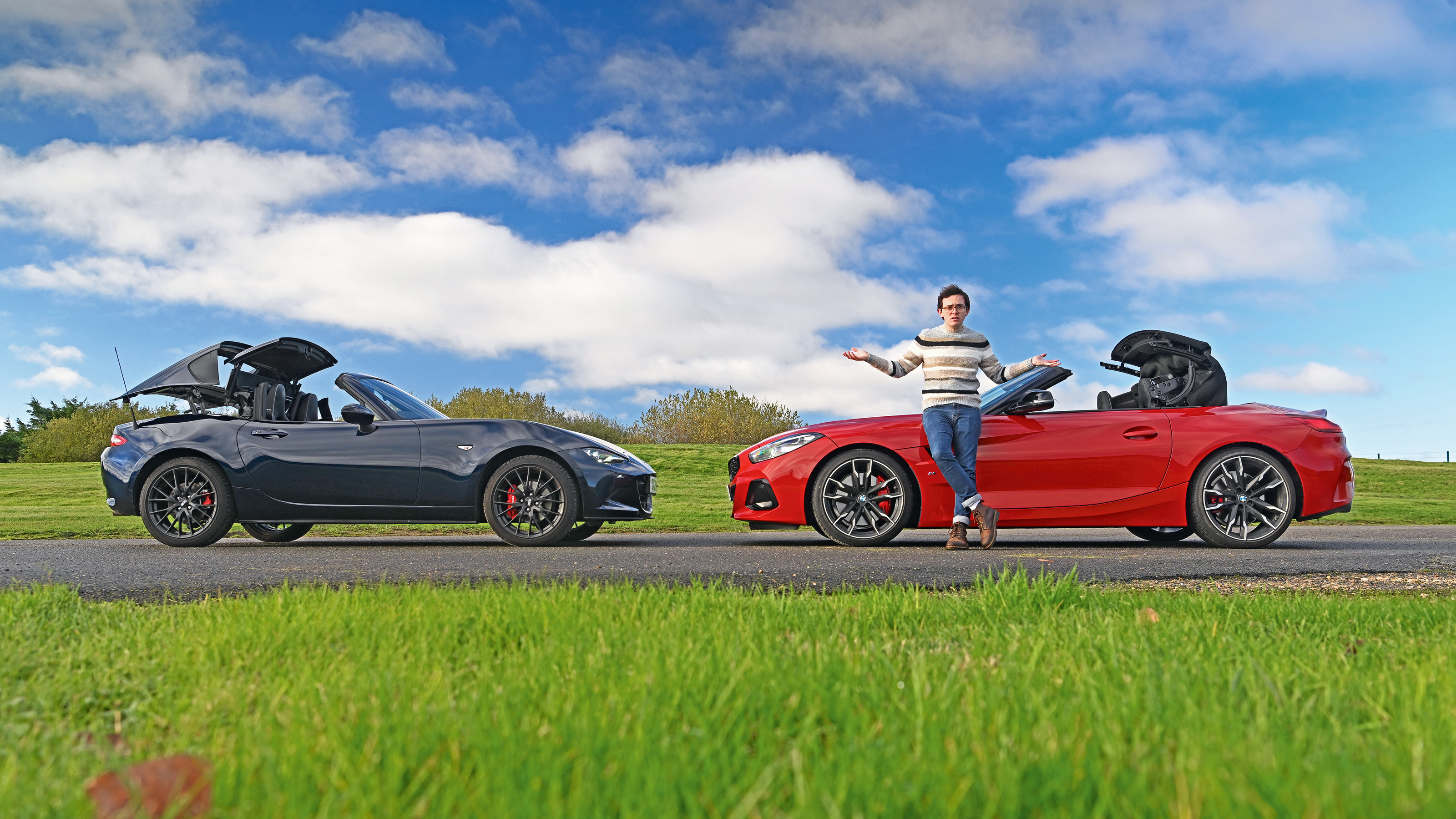 Auto Express consumer reporter Tom Jervis standing in front of a Mazda MX-5 and BMW Z4