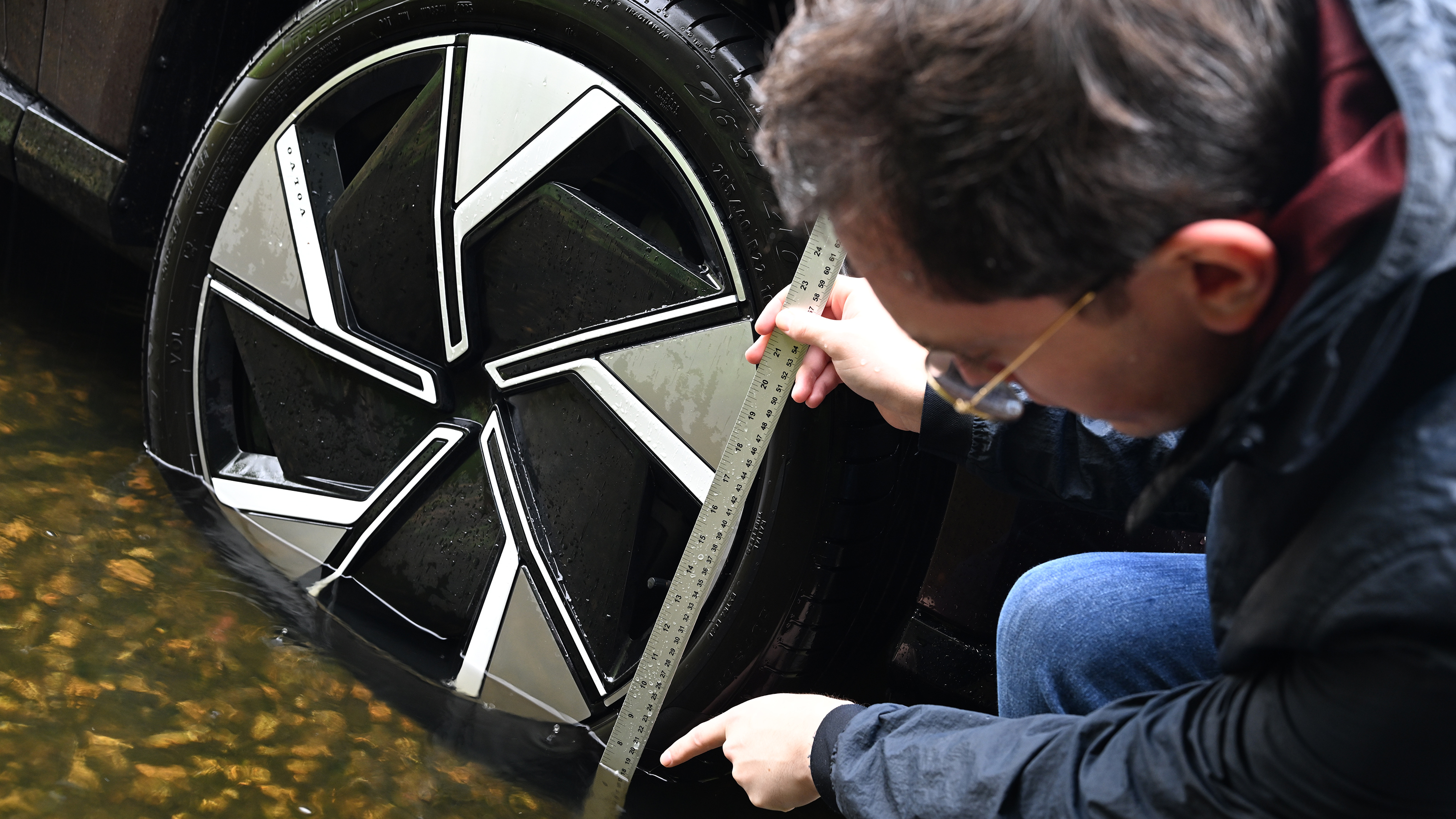 Auto Express consumer reporter Tom Jervis measuring water depth on a Volvo EX90 wheel