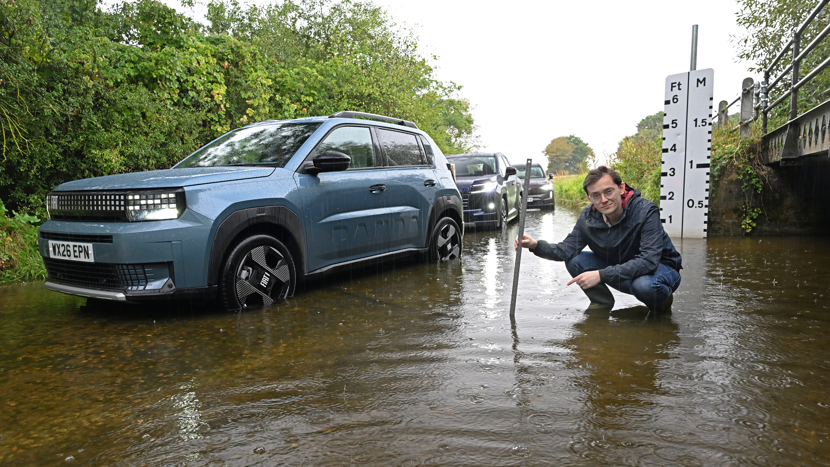 Auto Express consumer reporter Tom Jervis crouching next to a Fiat Grande Panda in ford water
