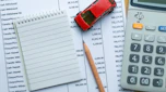 Calculator, model car, pencil and notebook on desk